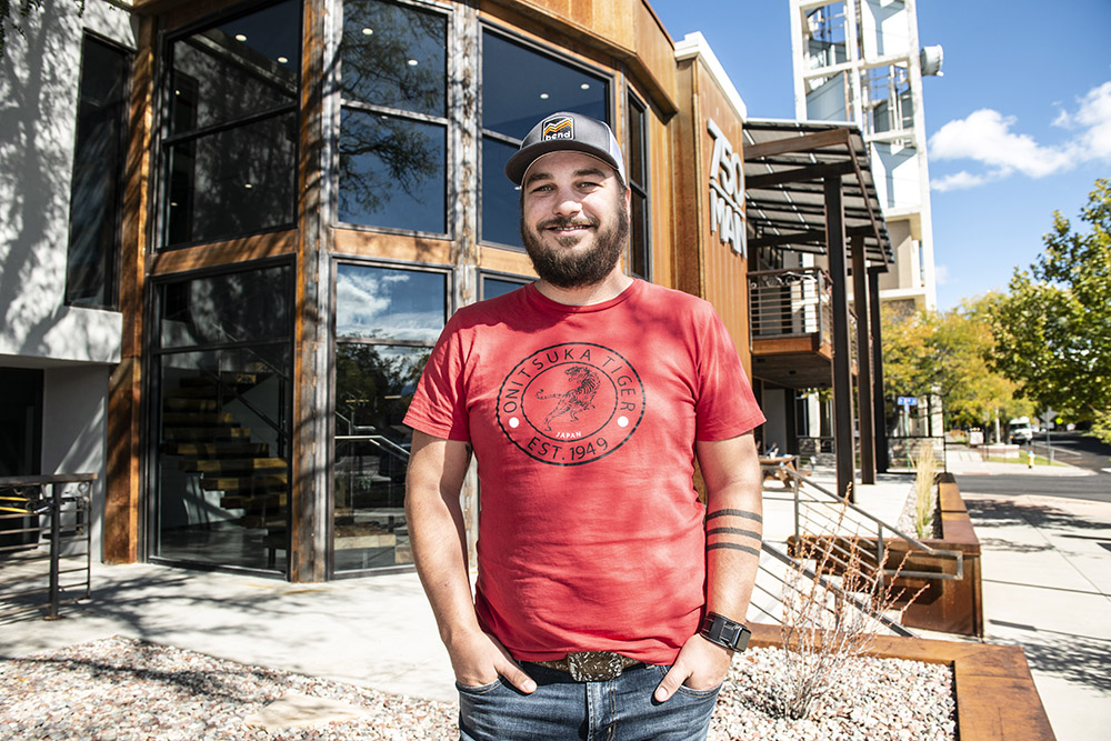 Bearded man in a red t-shirt outside a modern building, highlighting Rocky Mountain Commercial Real Estate in Grand Junction.