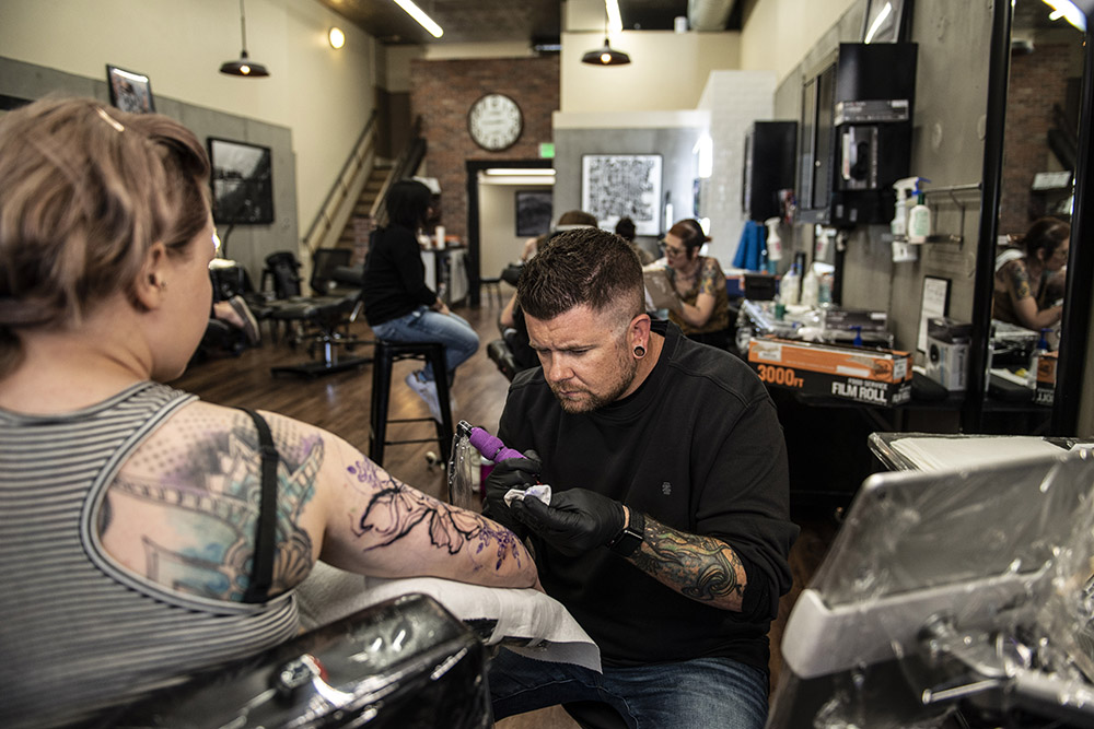 Tattoo artist working on a client’s arm with intricate designs in a vibrant studio, highlighting the creative atmosphere.