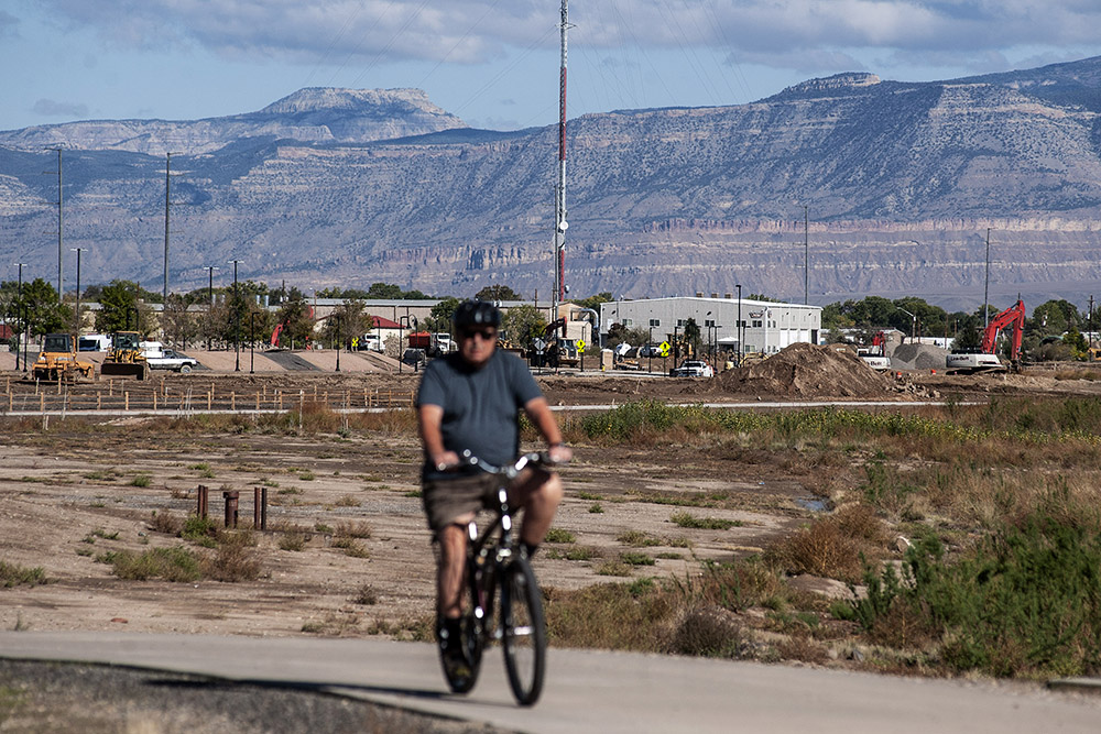 Cyclist on a path near construction in Grand Junction, with mountains and commercial real estate activity in the background.