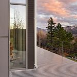 Modern commercial architecture with an outdoor deck, glass structure, trees, and mountain view in Alamosa County.