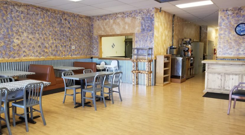 Interior view of a retail space featuring tables and chairs, with a decorative wall design and kitchen area visible, suitable for lease in Valley View Plaza, Delta, CO.