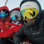 Three skiers in bright jackets on a snowy chairlift, highlighting outdoor activities in Colorado mountain towns real estate.