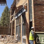 Construction worker in safety vest cleaning partially demolished building for Rocky Mountain Real Estate updates.