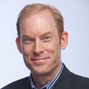 Portrait of a commercial real estate broker in a dark suit, smiling against a neutral background.