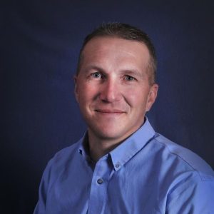A smiling man in a light blue shirt against a dark blue background, representing Rocky Mountain Commercial Real Estate.