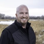 Smiling man in black vest standing in a snowy field, representing local brokers from Rocky Mountain Commercial Real Estate.