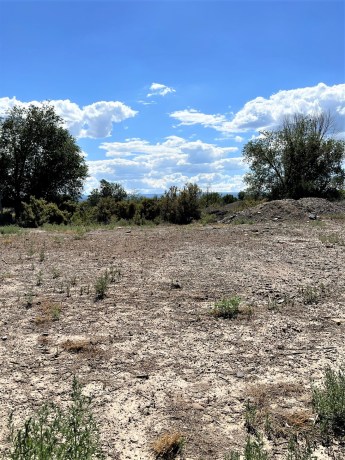 Vacant commercial land at TBD Lot 7 & 8 Hawk Parkway, Montrose, with sparse vegetation, blue sky, and distant trees, highlighting development potential in a booming business corridor.