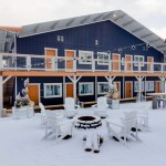 Loge Camp Motel in Breckenridge, Colorado, featuring a snowy outdoor seating area with white chairs around a fire pit, and a blue and orange building in the background.