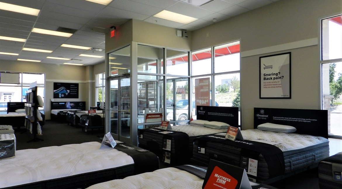 Commercial retail space interior showcasing various mattresses for sale, featuring signage for Mattress Firm, large windows, and a bright, open layout.