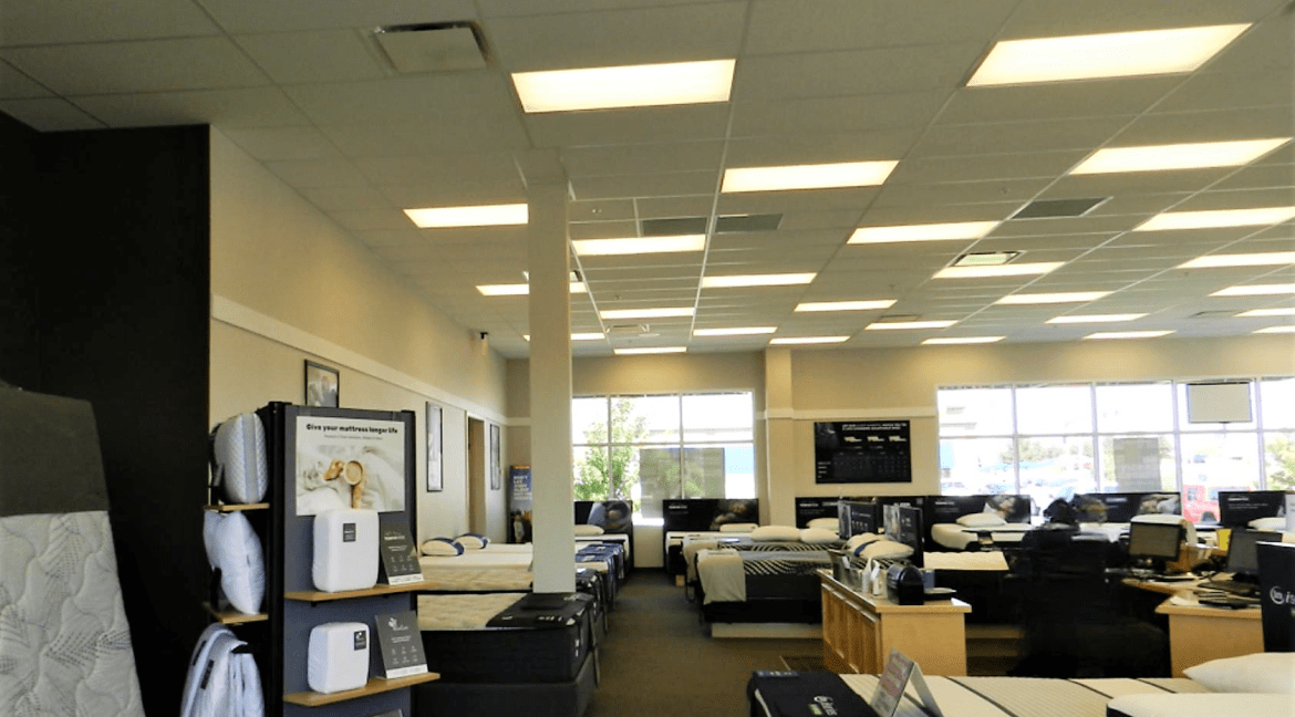 Commercial retail showroom interior featuring multiple mattress displays, bright lighting, and large windows, emphasizing the spacious layout suitable for a retail environment.
