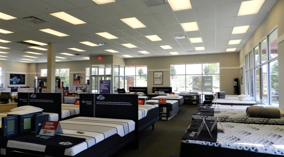 Interior of a commercial mattress showroom with multiple display beds, large windows, and promotional signage, highlighting retail space available for investment at 3501 Wolverine Dr, Montrose, Colorado.