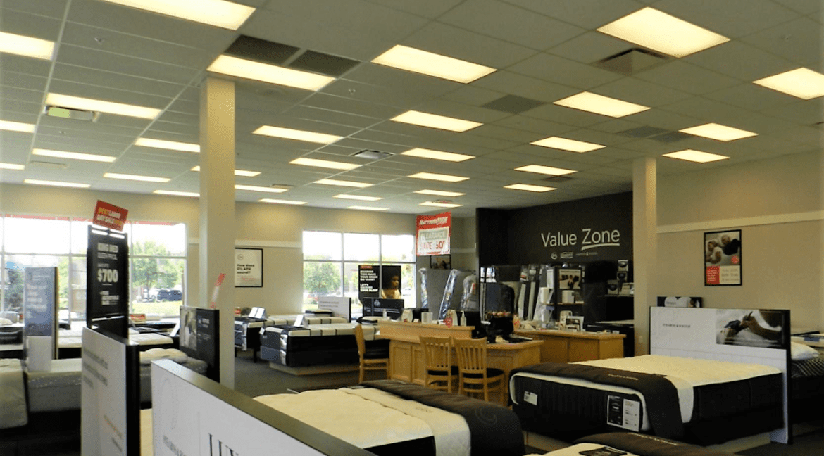 Interior of a commercial retail space featuring mattresses for sale, with signage indicating "Value Zone" and pricing tags, showcasing a well-lit showroom environment.