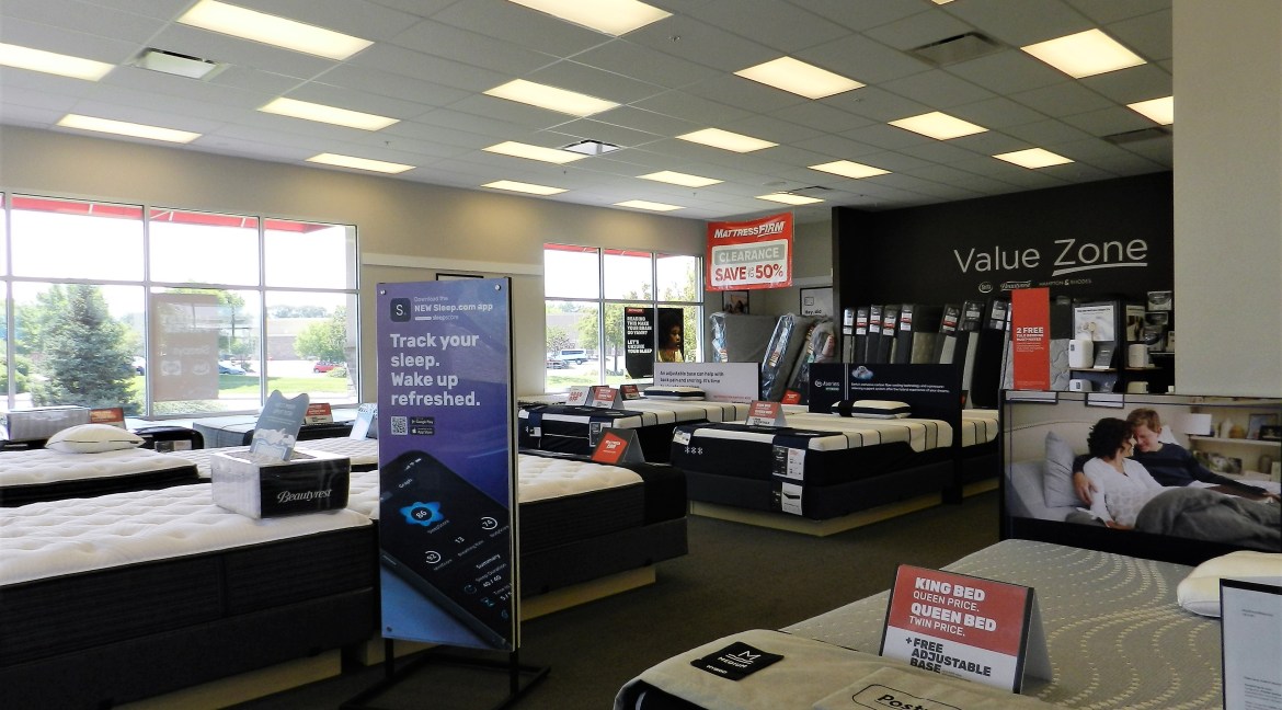 Mattress showroom featuring various mattress displays, promotional signage for Mattress Firm, and a sleep tracking app advertisement, emphasizing retail and investment opportunities in commercial real estate.