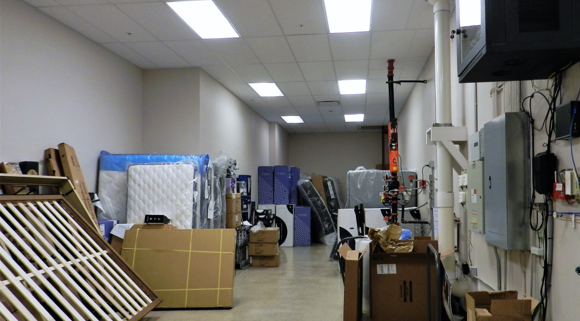 Storage area filled with boxes, mattresses, and furniture items, showcasing the interior of a commercial retail/office building for sale at 3501 Wolverine Dr, Montrose, Colorado.