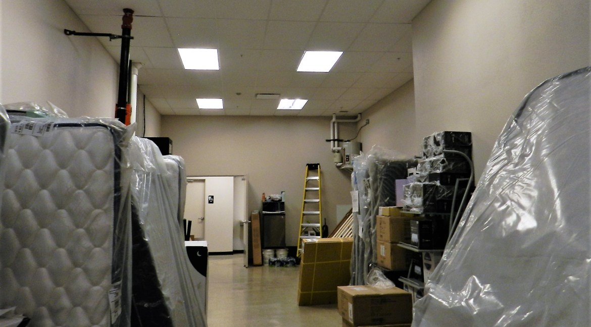 Storage area with stacked mattresses, boxes, and a ladder, showcasing the interior of a commercial retail/office building for sale at 3501 Wolverine Dr, Montrose, Colorado.