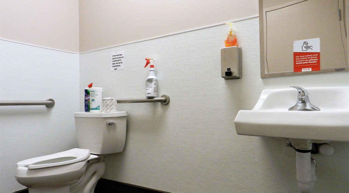 Restroom interior featuring a toilet, handwashing sink, cleaning supplies, and hand sanitizer, emphasizing cleanliness and accessibility for commercial property at 3501 Wolverine Dr, Montrose, Colorado.
