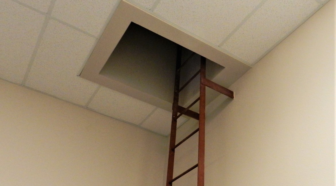 Ladder leading to a ceiling access panel in a commercial building, highlighting potential storage or maintenance space in a retail/office environment.