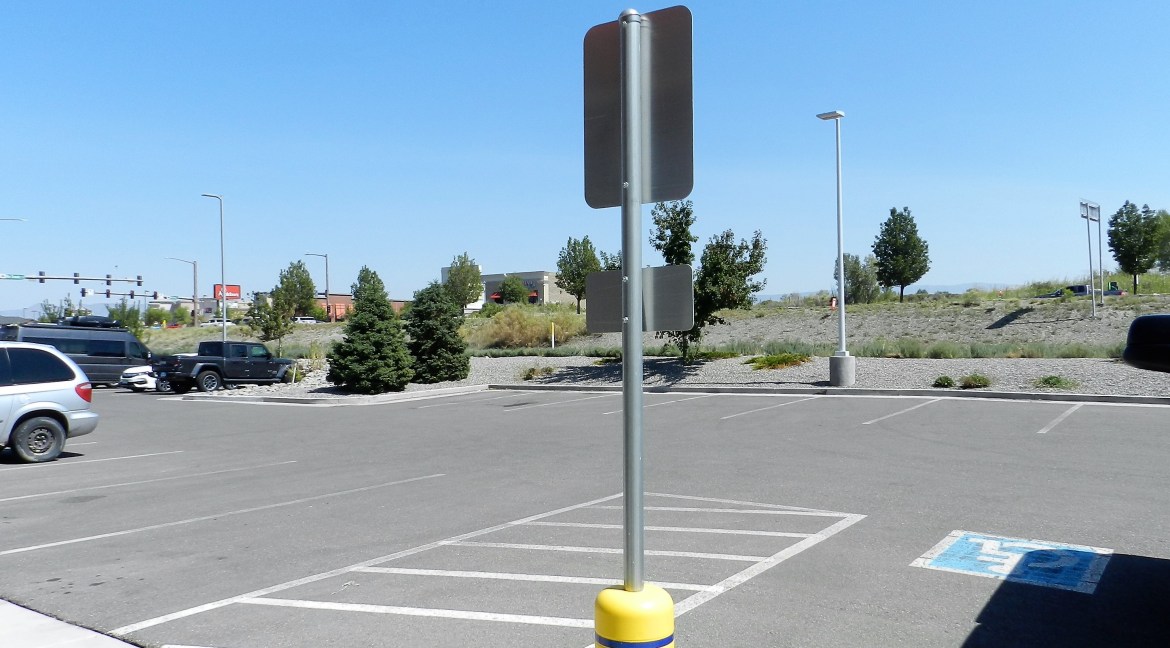 Parking lot view at commercial property on Wolverine Drive, featuring traffic signage and landscaped area with trees, highlighting accessibility and location near busy retail corridor.