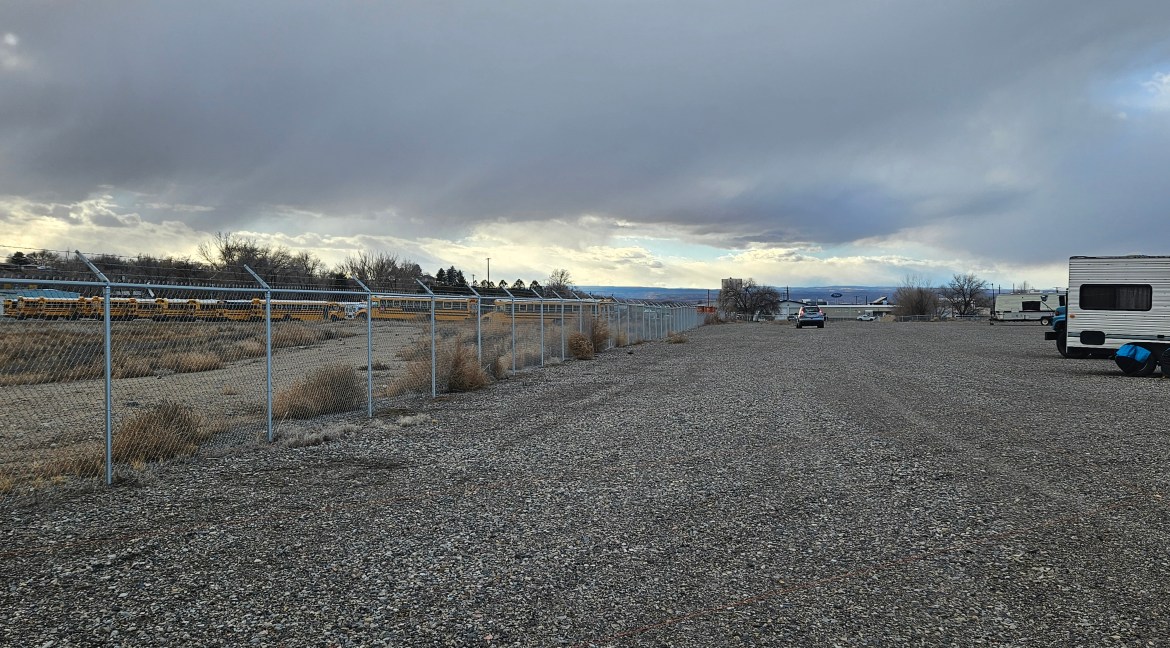 Fenced commercial land with gravel surface, adjacent to school buses, near 65 Circle Dr., Delta, Colorado, suitable for development or storage facility.