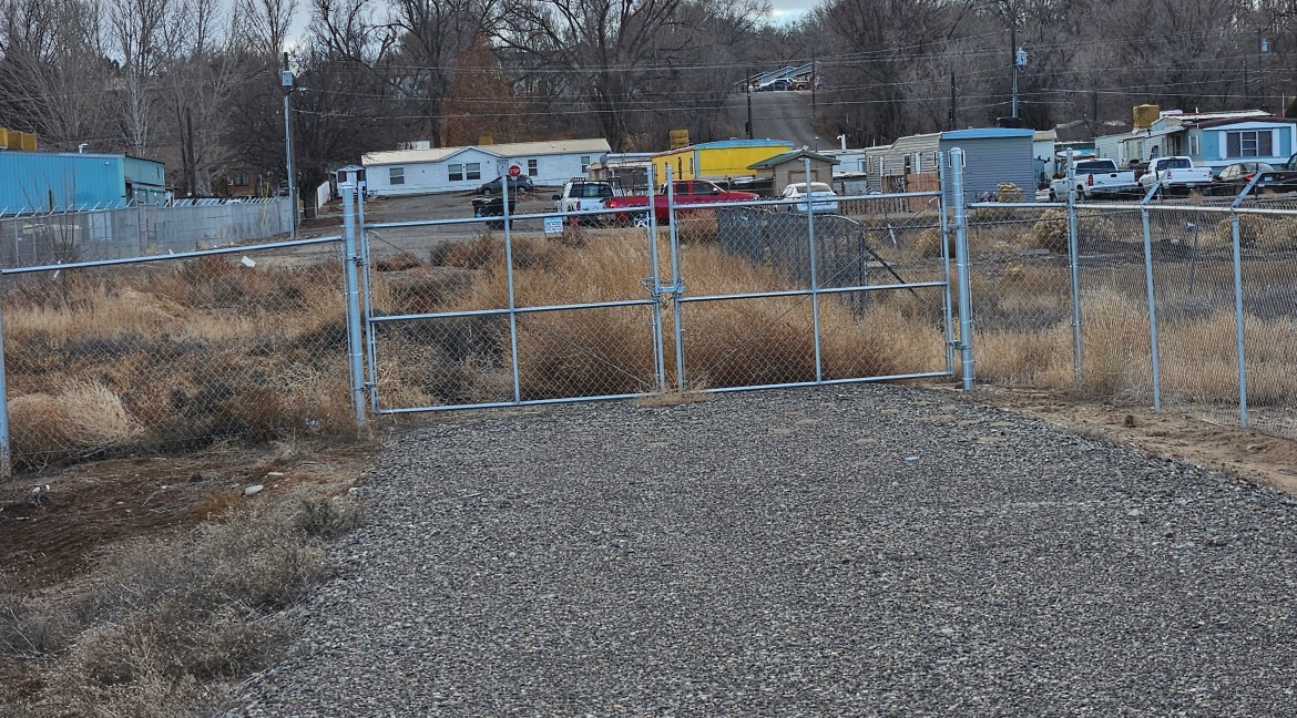 Fenced entryway leading to a partially improved 4.34-acre commercial parcel with B-3 zoning at 65 Circle Dr., Delta, Colorado, surrounded by residential and commercial structures.
