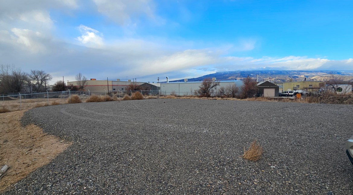 4.34-acre commercial land for sale at 65 Circle Dr., Delta, CO, featuring B-3 zoning, gravel surface, and adjacent buildings.