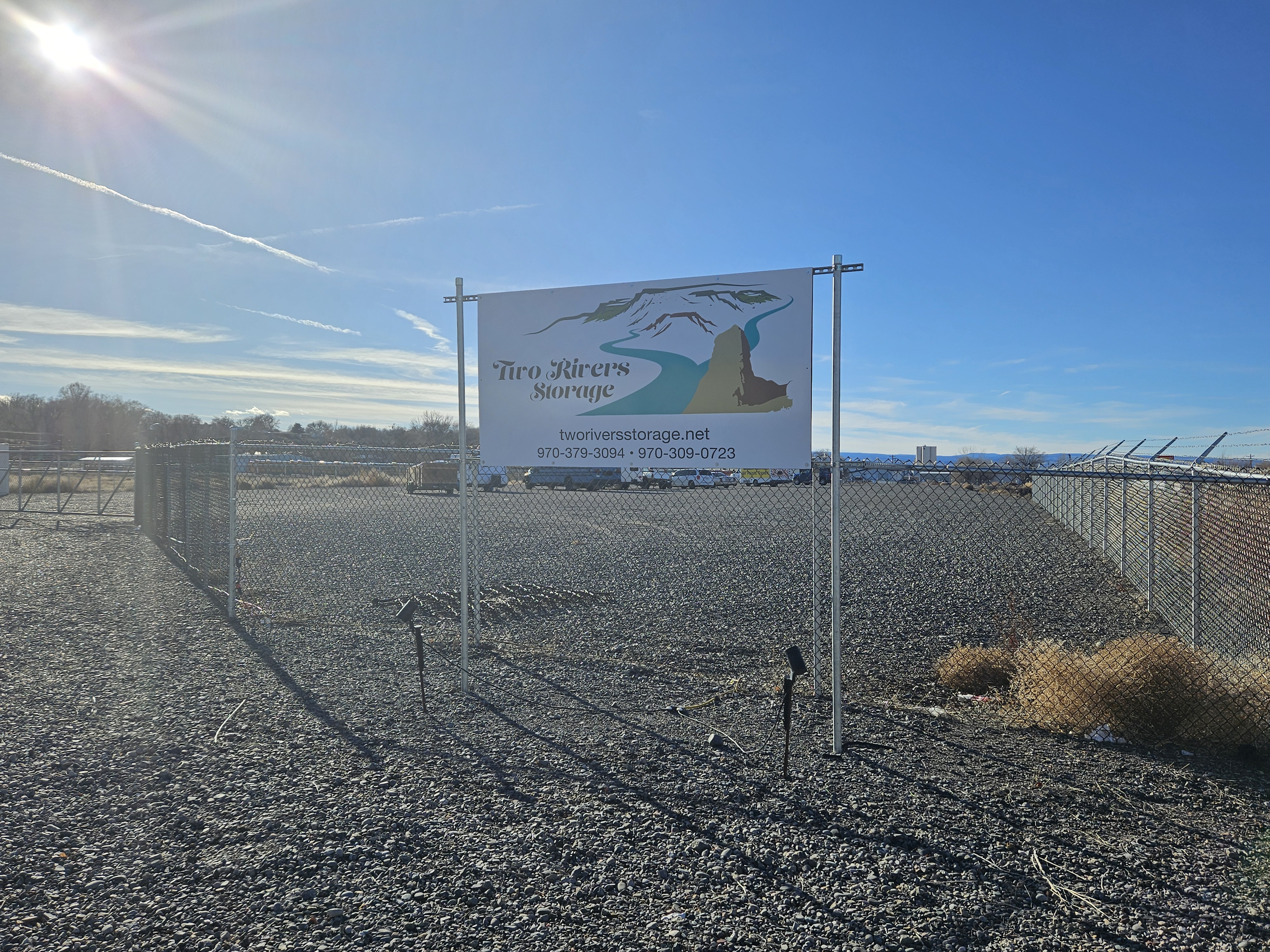 Tiro Rivers Storage sign in fenced commercial lot, Delta, Colorado, with blue sky and distant mountains, indicating potential development for storage facility.