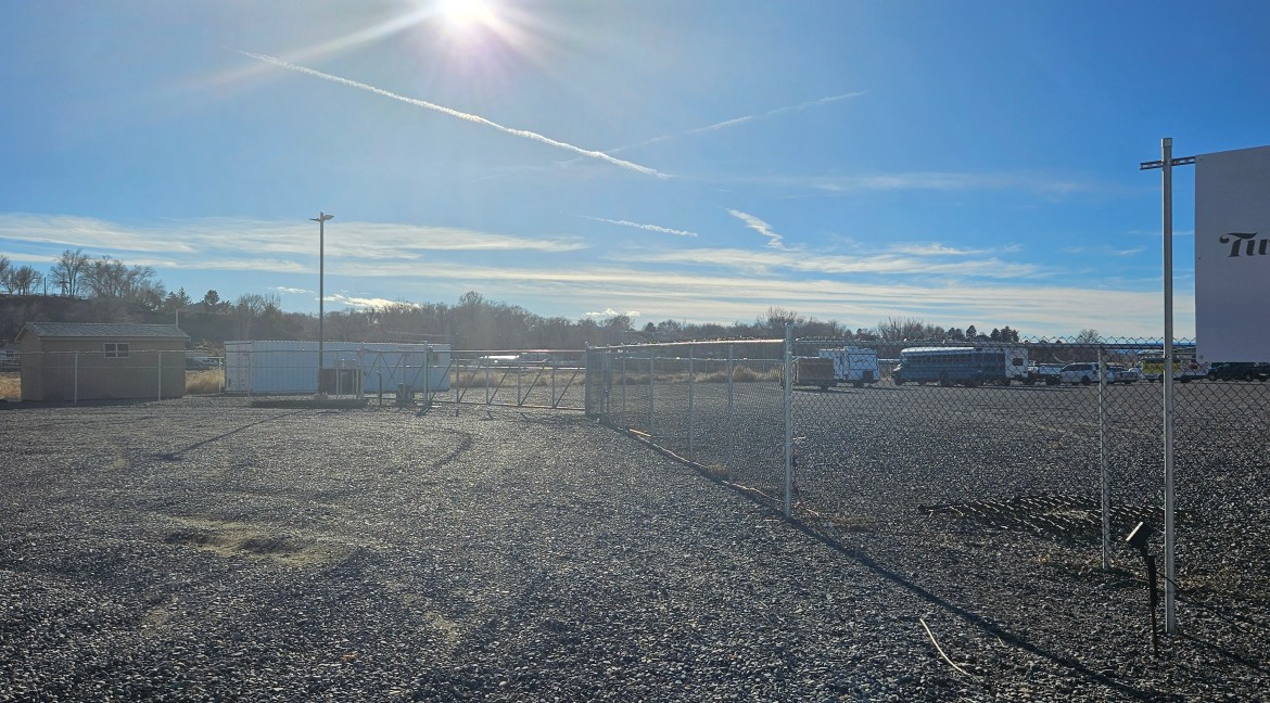 Partially improved commercial land for sale at 65 Circle Dr., Delta, Colorado, featuring gravel lot, fenced perimeter, storage units, and surrounding commercial properties.