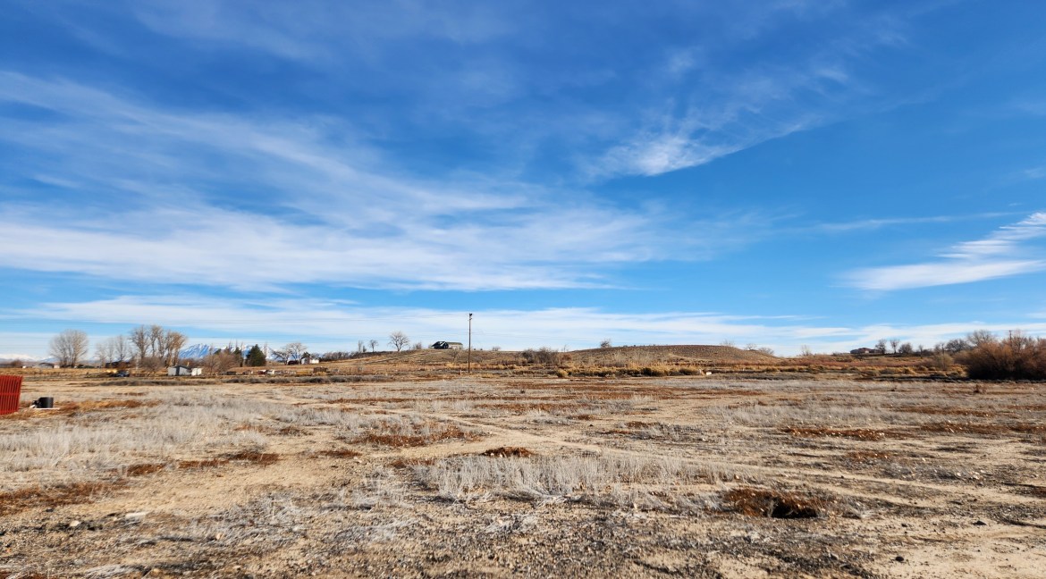 14.84-acre residential development land for sale in Delta, Colorado, featuring open terrain and distant hills under a clear blue sky.