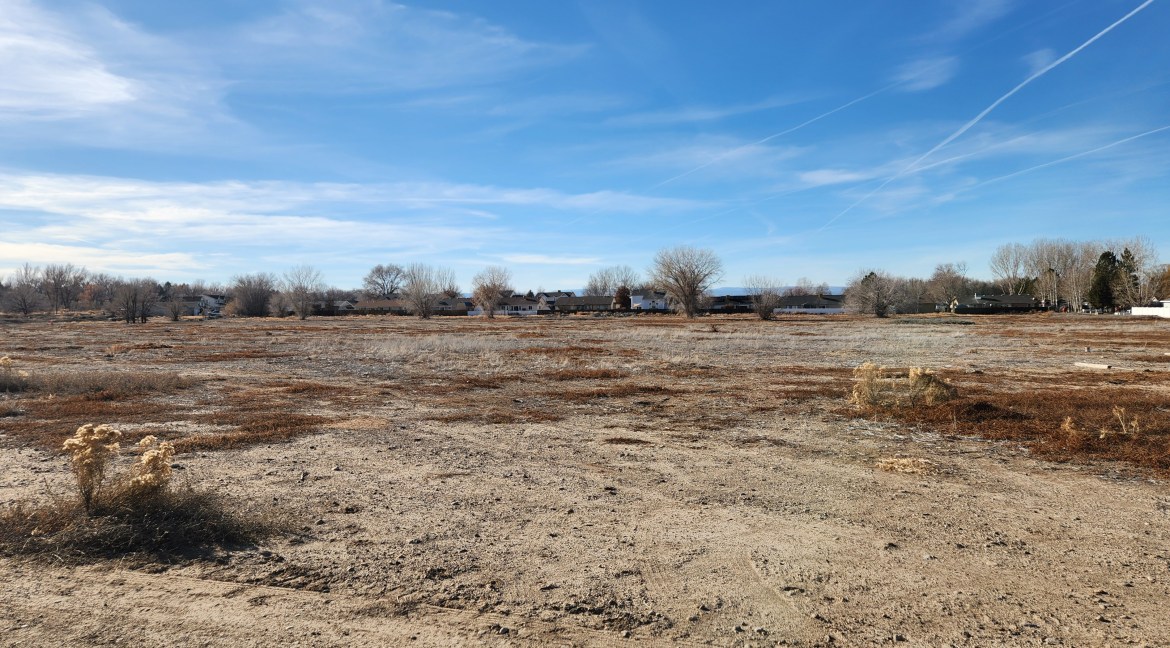Vacant 14.84-acre residential development land in Delta, Colorado, featuring sparse vegetation and distant homes under a clear blue sky, showcasing investment potential for buyers.