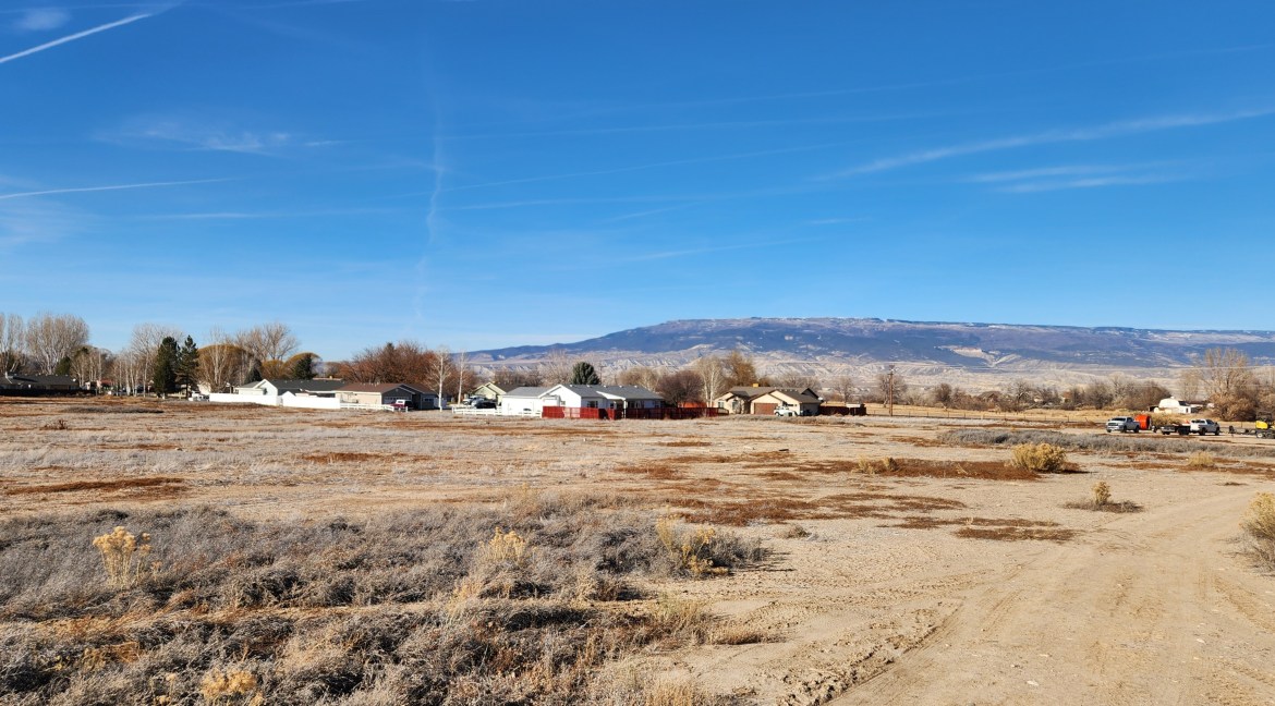 14.84-acre residential development parcel in Delta, Colorado, featuring surrounding homes, open land, and distant mountains under a clear blue sky.