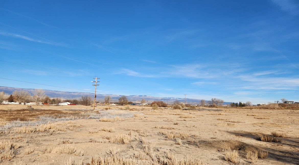 14.84-acre residential development parcel in Delta, Colorado, featuring dry land with sparse vegetation, power lines, and distant mountains under a clear blue sky.