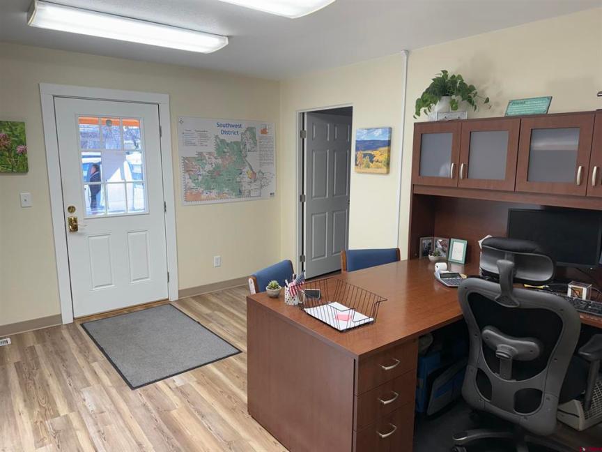 Office interior featuring a wooden desk with a computer, two blue chairs, a wall map of the Southwest District, and a welcoming entrance door, reflecting a professional environment suitable for a commercial property investment opportunity in Alamosa, Colorado.