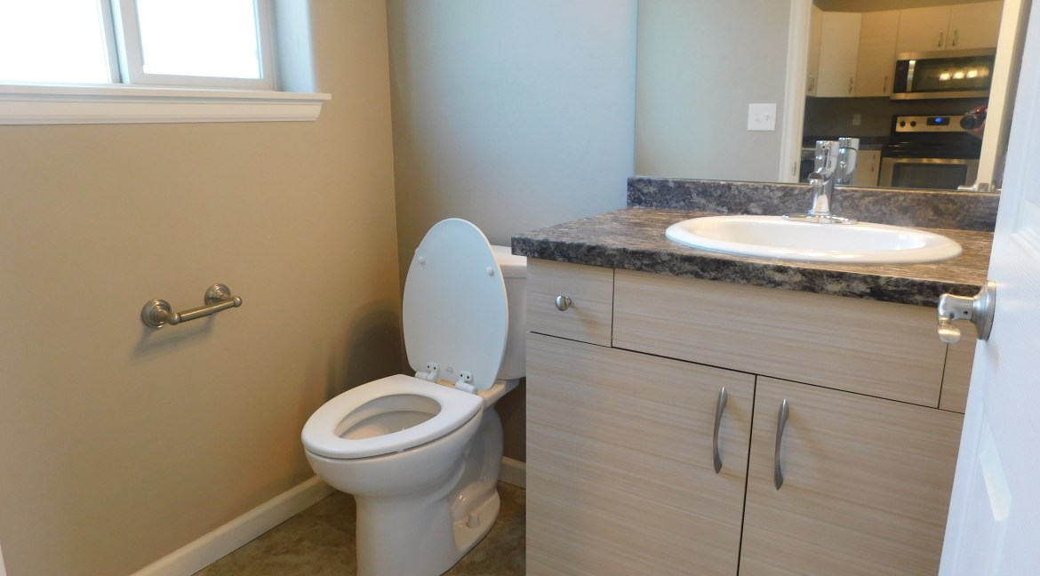 Modern half-bathroom featuring a toilet, sink with granite countertop, and neutral wall colors, part of a contemporary townhome unit for sale at 1534 Poplar Drive, Grand Junction, CO.