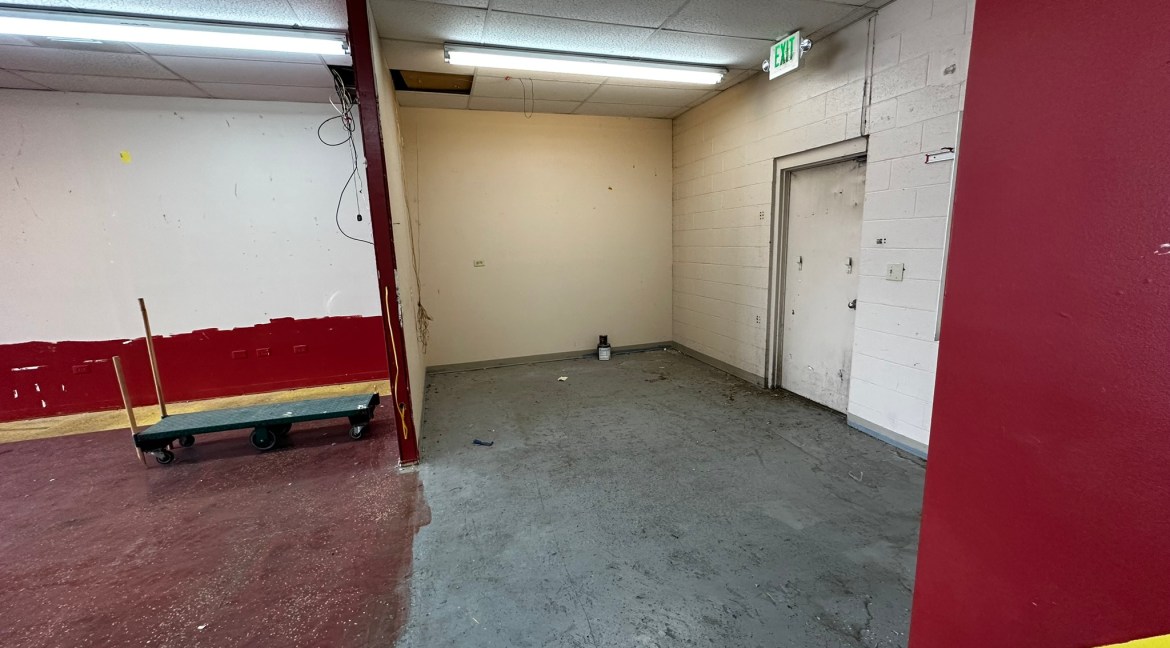 Retail unit interior at Coronado Plaza Shopping Center, featuring a partially painted wall, concrete flooring, and a hand truck, ideal for commercial leasing in Clifton, Colorado.